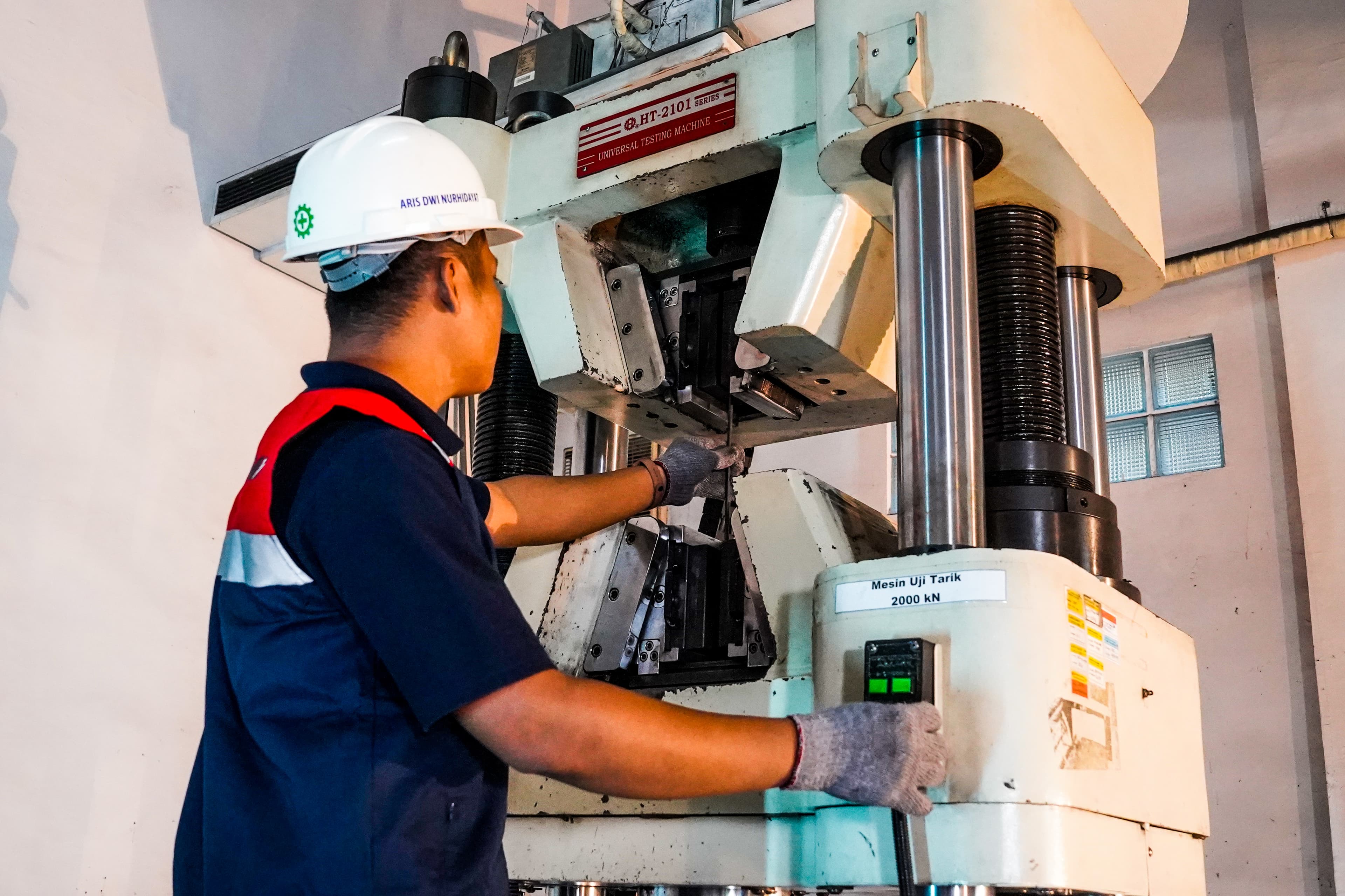 Operator menjalankan mesin uji tarik di ruang pengujian.