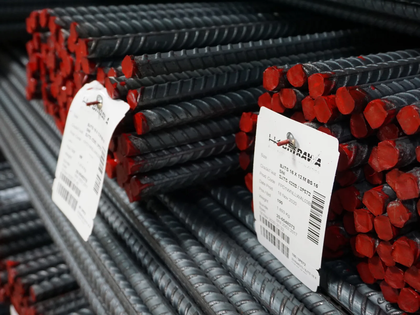 Bundel baja tulangan ulir bersirip dengan ujung batang dicat merah dan label identitas produk tergantung di sisi bundel.