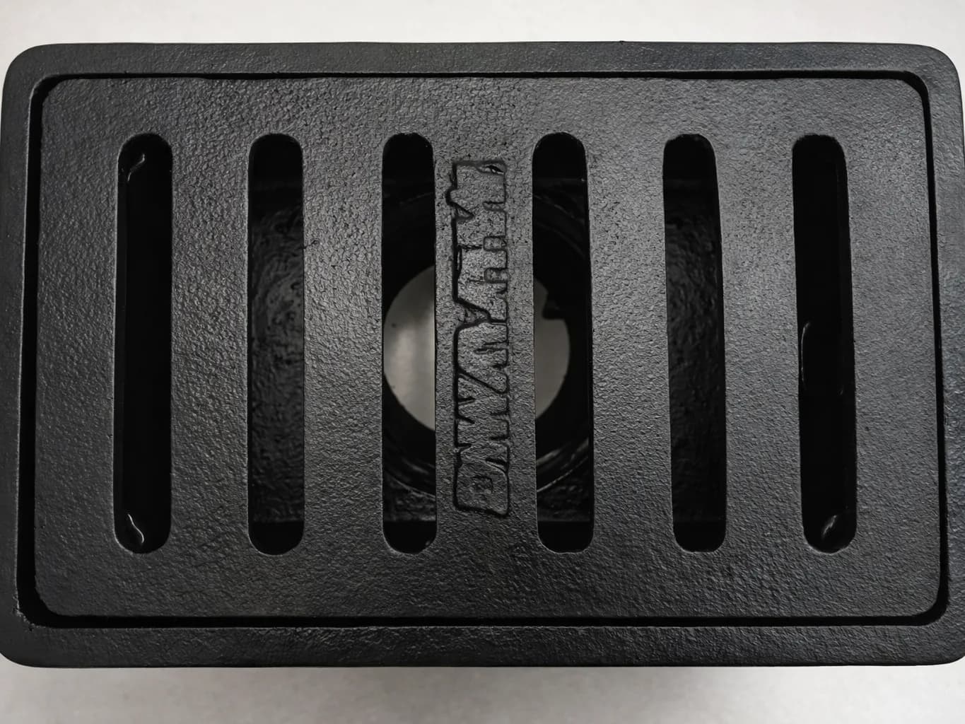 Tampak atas deck drain besi cor berwarna hitam dengan enam bukaan memanjang dan tulisan Bhirawa yang dicor timbul di tengah.